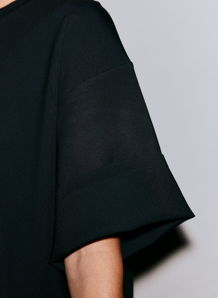 Lähikuva henkilön käsivarresta yllään musta Luxe Boxy Short Sleeve -toppi. [M-170cm]