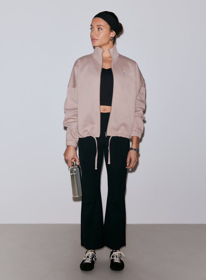 Nainen yllään mustat Luxe Kick Flare Leggings -trikoot, musta croptop ja vaaleanpunainen vetoketjullinen takki, pitäen vesipulloa. [36-170CM]