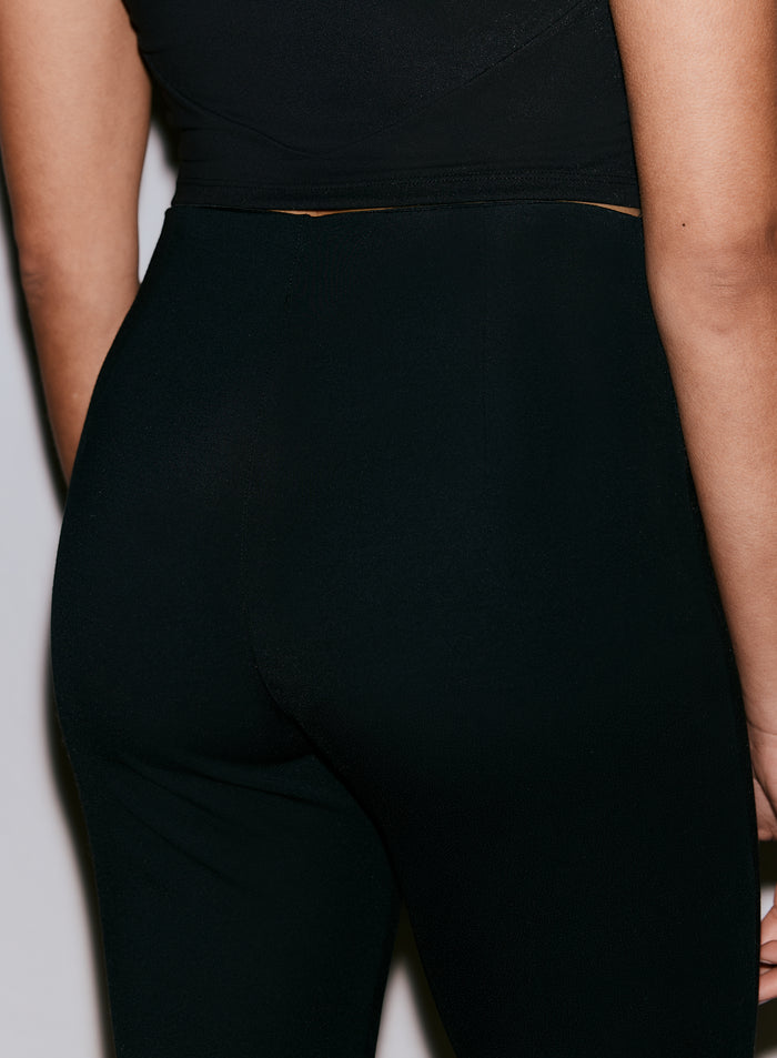 Lähikuva henkilön selästä, jolla on yllään mustat Luxe Kick Flare Leggings -leggingsit, korostaen istuvuutta ja kangasta [36-170CM]