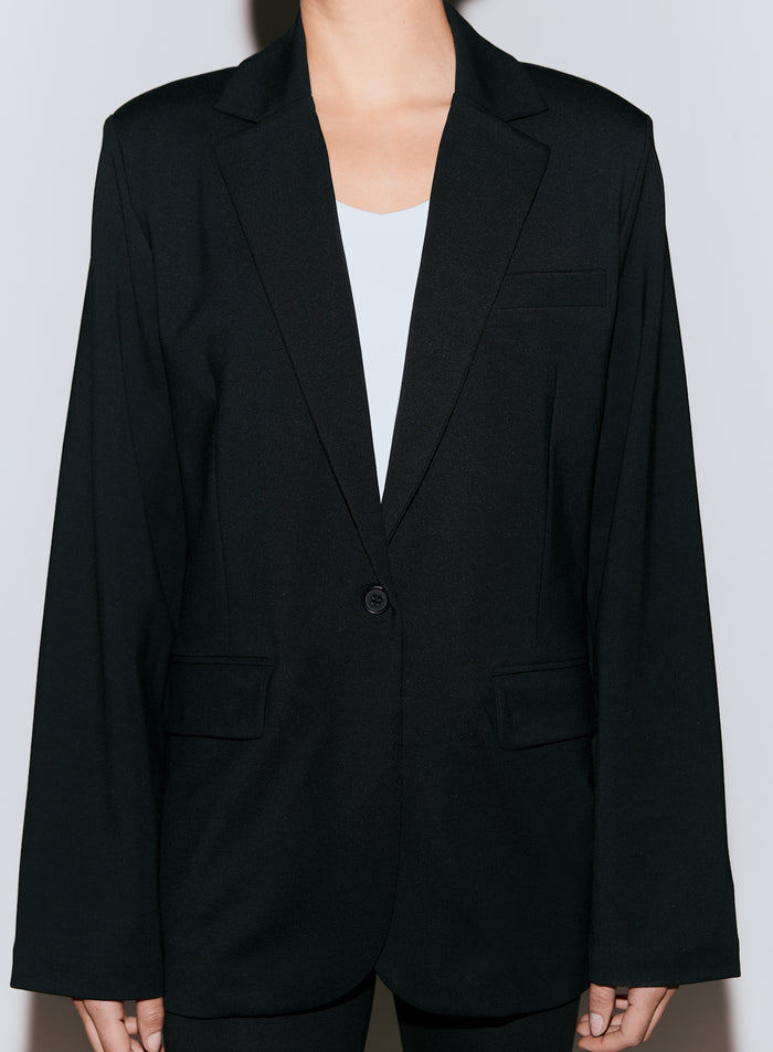 Lähikuva mustasta Luxe Relaxed Blazer -bleiseristä valkoisen topin päällä, näyttäen yksinappikiinnityksen ja etutaskut [40-170cm]
