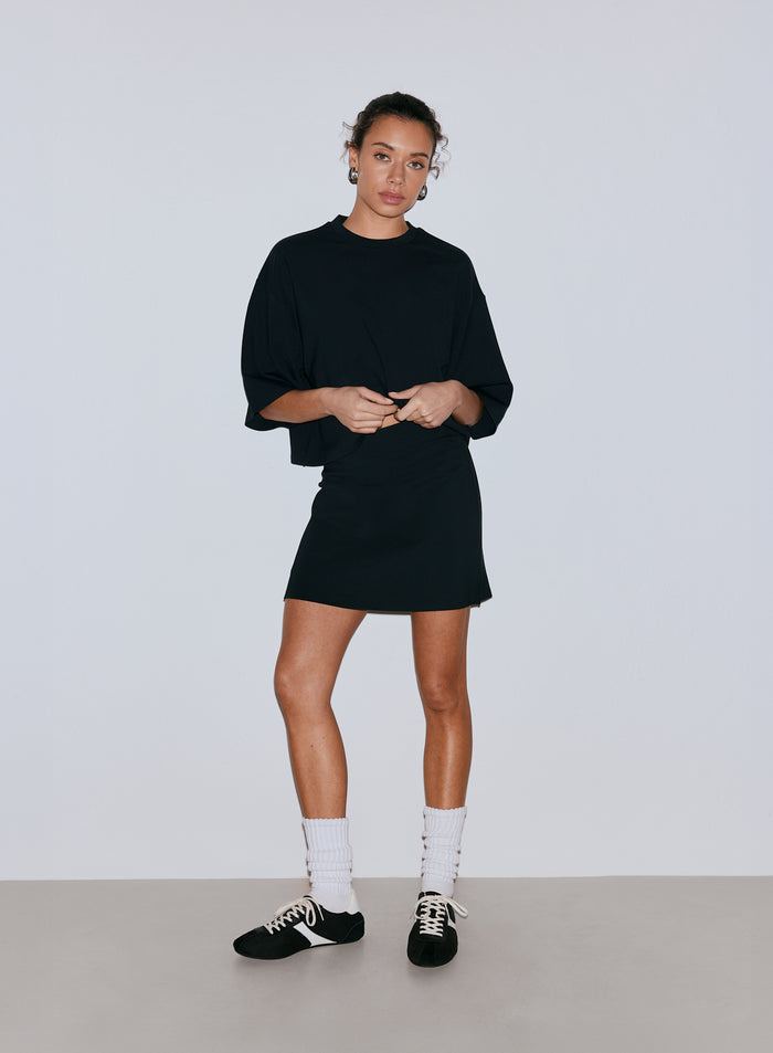 Naispuolinen malli yllään musta oversized toppi ja musta minishortsihame, valkoiset sukat ja lenkkarit. [36-170CM]
