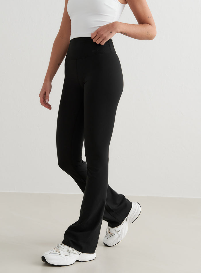 Mustat korkeavyötäröiset aim'n Sense Flare Tights pehmeällä kankaalla, levenevillä lahkeilla ja valkoisilla lenkkareilla.