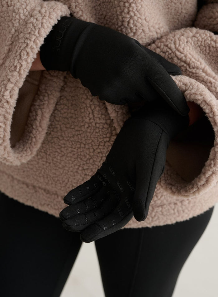 Mustat lämpökäsineet pitopainatuksella ja aim'n-logolla beigen fleece-takin kanssa.