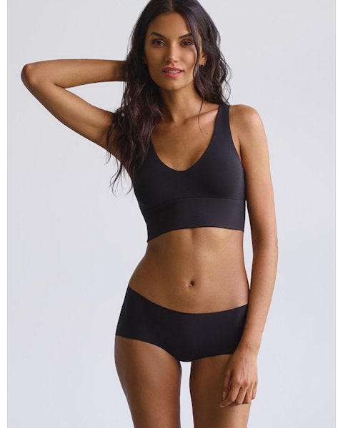A woman wearing black hipster underwear, standing with one hand raised to her head.