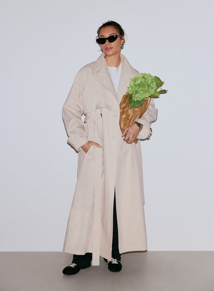 Nainen yllään Café Au Lait Femme Trenchcoat -trenssitakki, mustat aurinkolasit ja pitäen käsissään kimpun vihreitä kukkia [M-170cm]