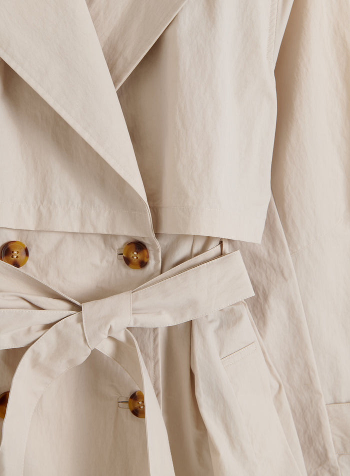Café au lait aim'n Femme Trenchcoat -takin yksityiskohta kilpikonnakuvioisilla napeilla, vyöllä ja myrskyläpillä.