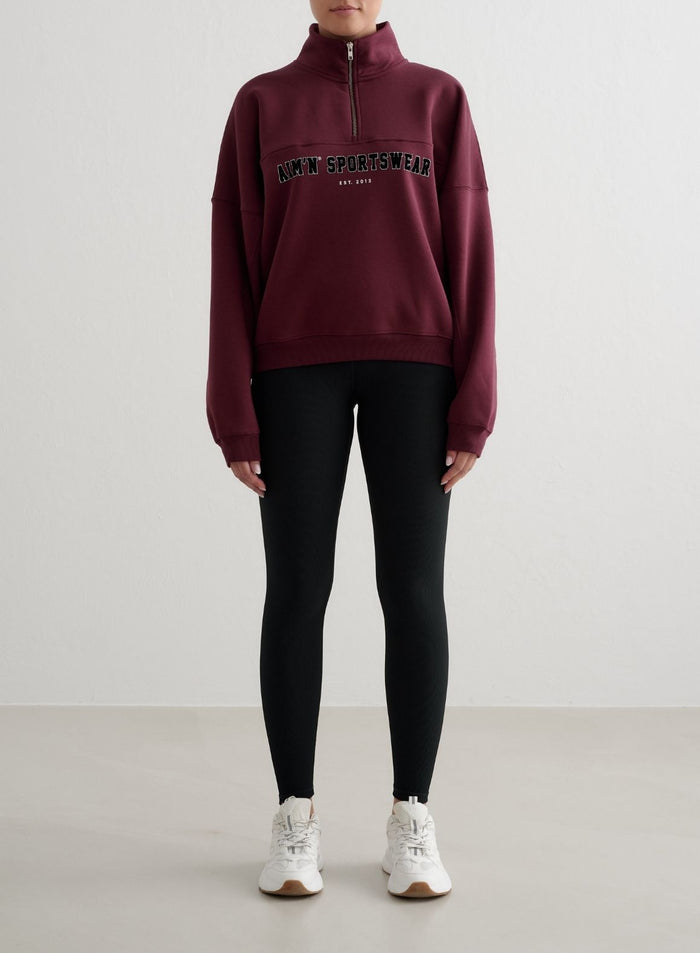 Kirsikanpunainen aim'n Varsity Sweat Half Zip pystykauluksella ja varsity-kirjailulla sekä mustat leggingsit.