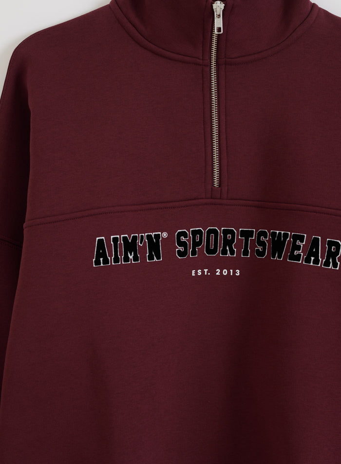 Kirsikanpunainen Varsity Sweat Half Zip -collegepaita pystykauluksella ja aim'n sportswear -printillä.