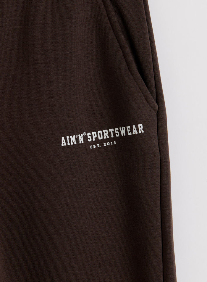 Suklaanruskeat Classic Sweatpants -collegehousut, joissa on sivutasku ja valkoinen aim'n-logo pehmeällä jerseyllä.