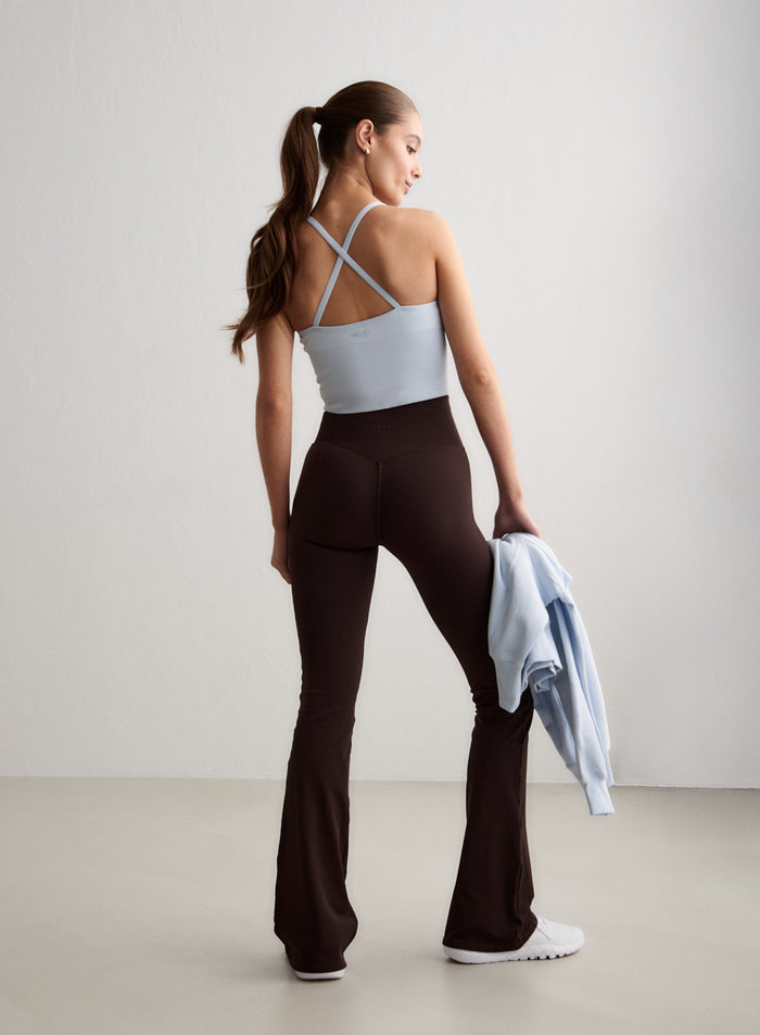 Nainen takaapäin yllään Chocolate Shape Seamless Flare Tall Tights -trikoot ja vaaleansininen toppi, kädessään vaaleansininen collegepaita. [S-174CM]
