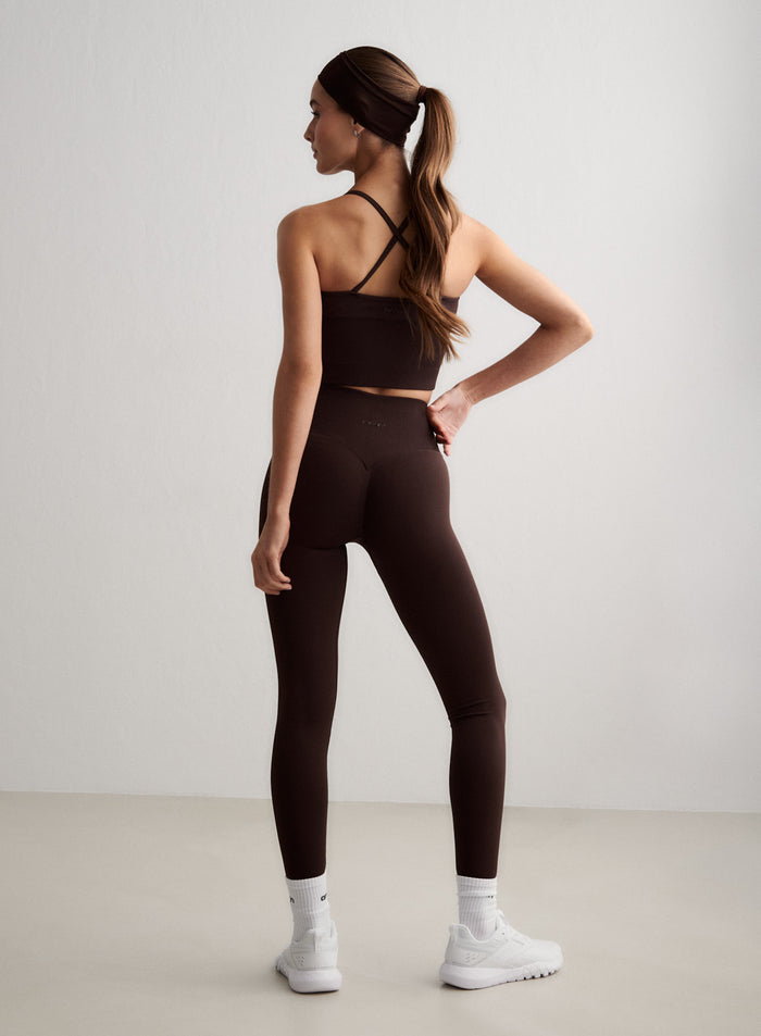 Nainen takaapäin yllään suklaanruskeat Shape Seamless Tall Tights -trikoot ja yhteensopivat urheiluliivit [S-174cm]
