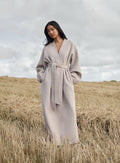 Rento aim'n Wool Coat värissä Dark Clay pitkällä siluetilla ja vyötärövyöllä ulkona pellolla.