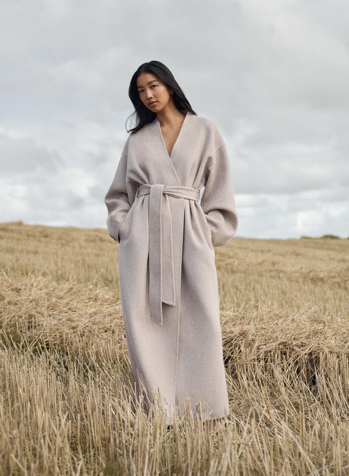 Rento aim'n Wool Coat värissä Dark Clay pitkällä siluetilla ja vyötärövyöllä ulkona pellolla.