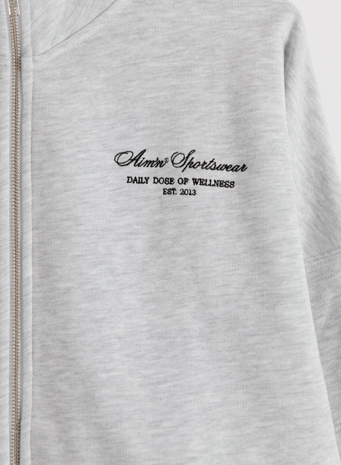 Vaaleanharmaa melange Script Zip Jacket, jossa on aim'n-printti rinnassa ja täyspitkä vetoketju.