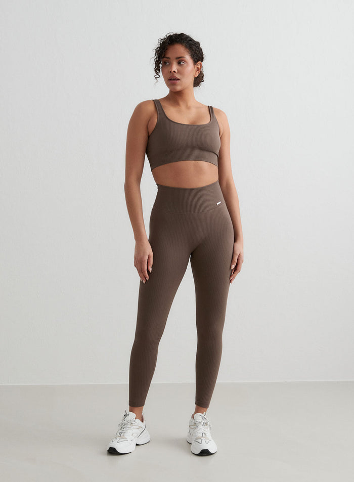 Nainen pukeutuneena ruskeaan aim'n ribbed seamless -settiin, jossa on pitkät trikoot ja urheiluliivit.