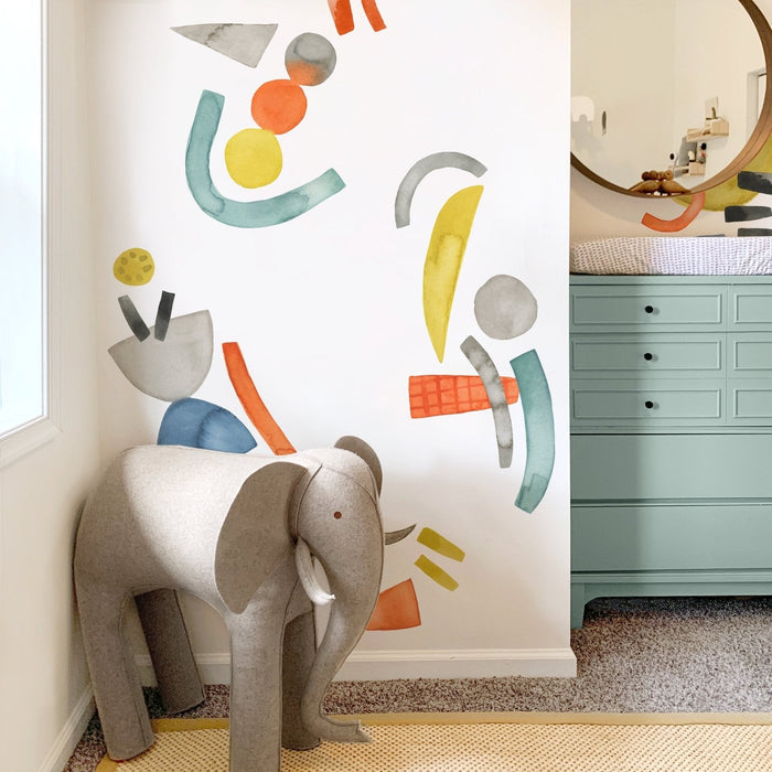Modern baby nursery corner with gray elephant stool, colorful abstract watercolor wall decals, mint teal changing dresser with round mirror and patterned changing pad