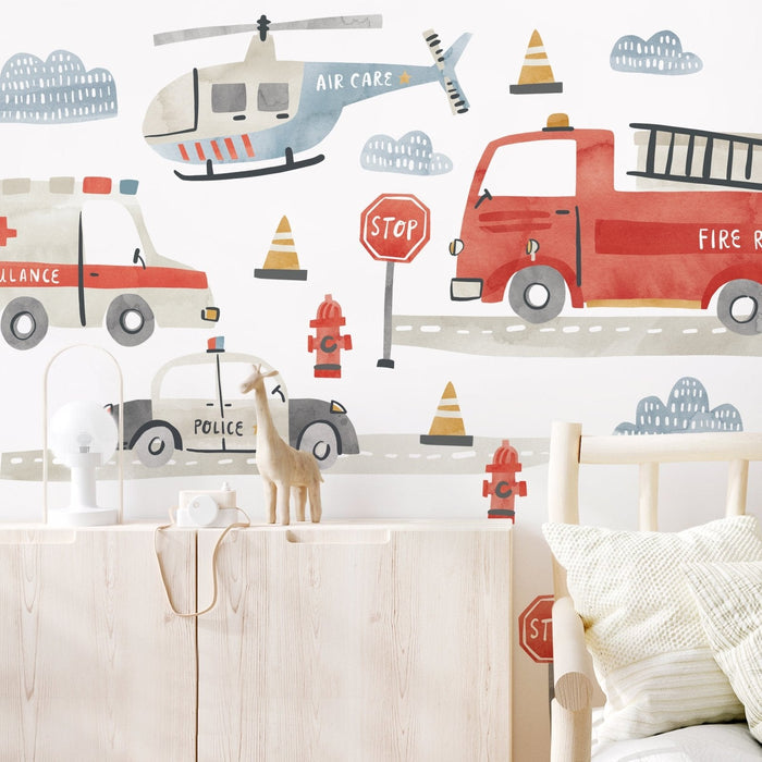 Watercolor children's room wallpaper featuring a red fire truck, ambulance, police car and rescue helicopter with stop signs, fire hydrants and traffic cones — nursery transportation mural wall decal