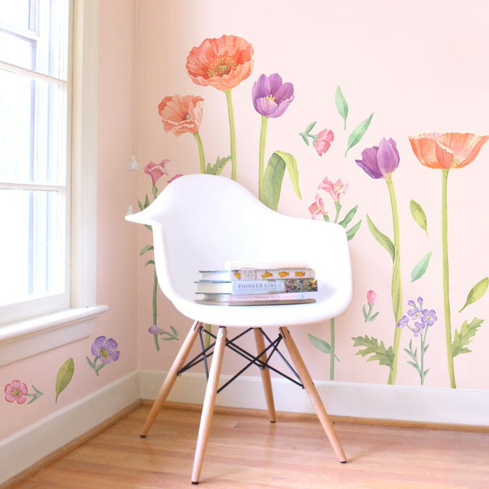 White mid-century modern chair with wooden legs in a sunlit nursery featuring pink walls, watercolor floral wall decals and a stack of children's books — pastel Scandinavian kids room decor