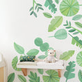 Nursery changing shelf with plush teddy bear, green tropical leaf wall mural and patterned pillow, baby room decor