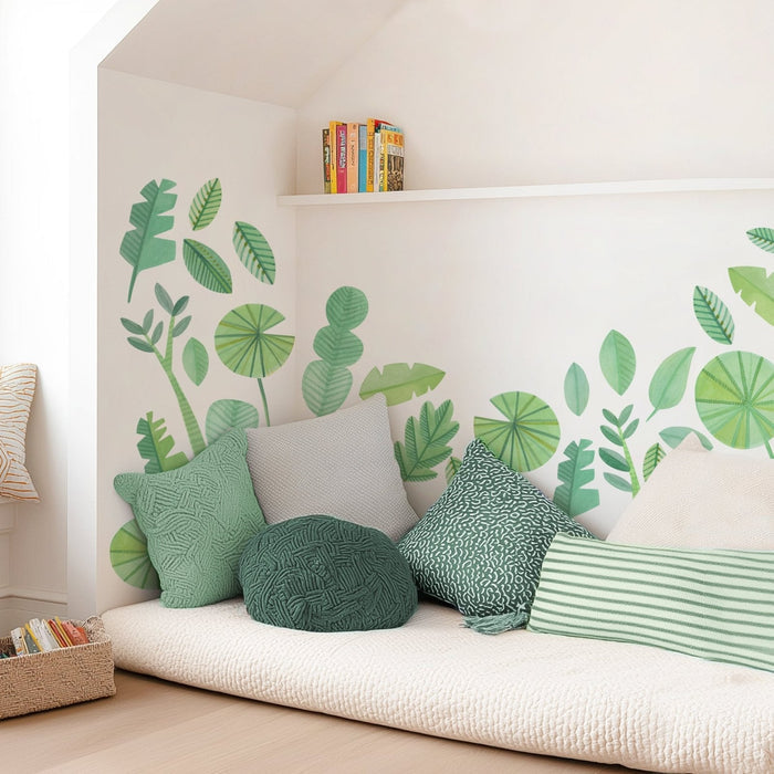 Cozy reading nook with green botanical leaf wall decals, textured green and striped throw pillows on a cream floor mattress, wicker book basket and minimalist white shelf