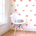 Minimalist reading nook with white Eames-style chair, wood legs, stack of books and pink poppy wall decals by a sunlit window