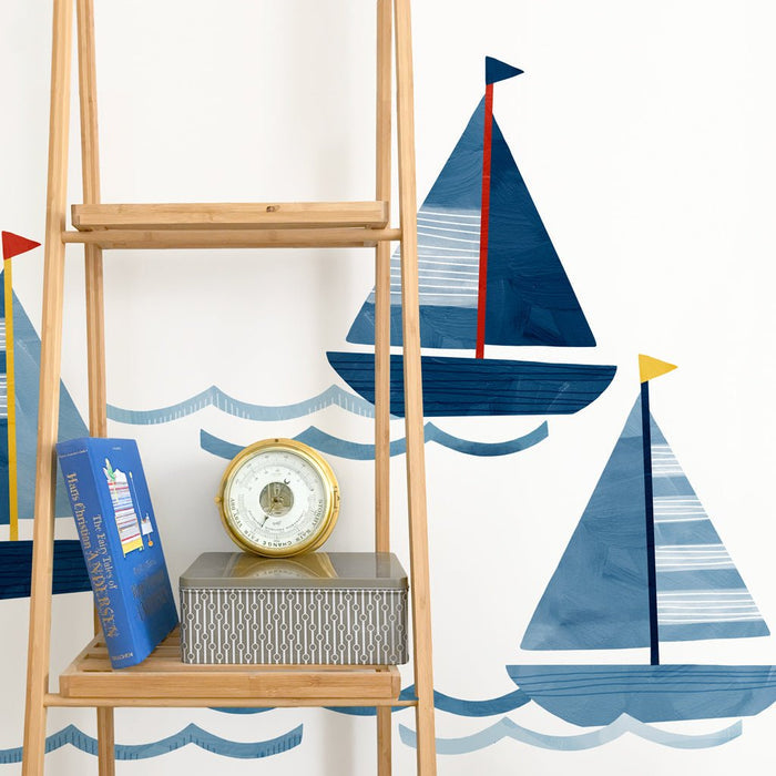 Children's nautical nursery wall with blue sailboat decals and waves, wooden ladder shelf with brass marine barometer, book and tin