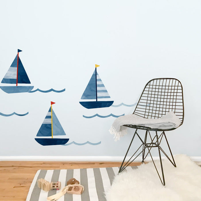 Nursery decor: coastal kids room with blue sailboat wall decals, modern wire chair with gray throw, striped rug and wooden toys