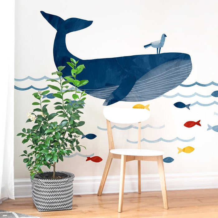 Blue whale wall decal nursery mural for kids room featuring ocean-themed colorful fish and bird accents above a white wooden chair and potted plant