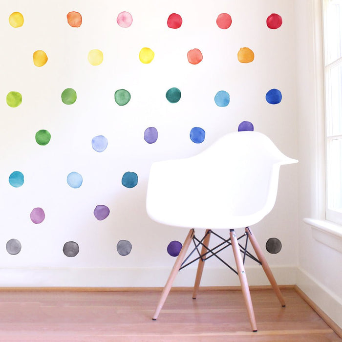 White modern Eames-style chair with wooden legs on light hardwood floor beside window, colorful watercolor polka dot wall decals in minimalist nursery