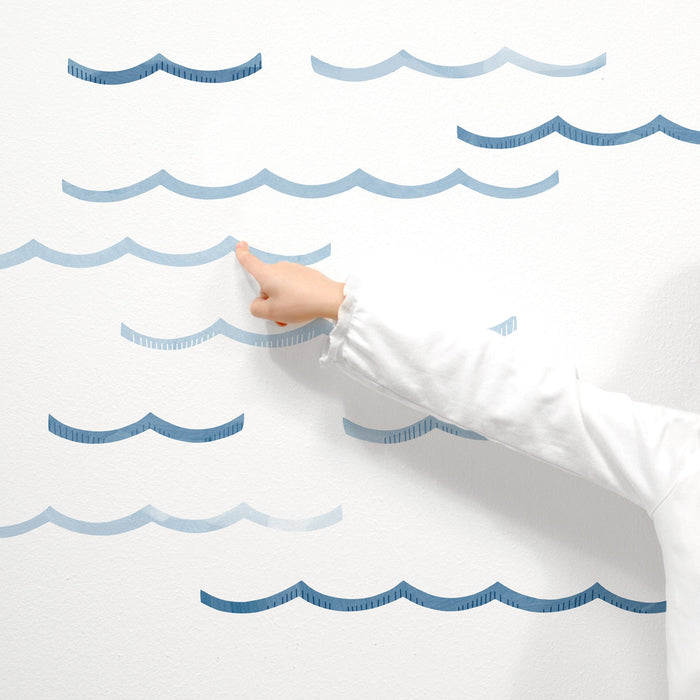 Child's hand pointing at blue wave wall decals on white wall, ocean-themed nursery and kids room decor