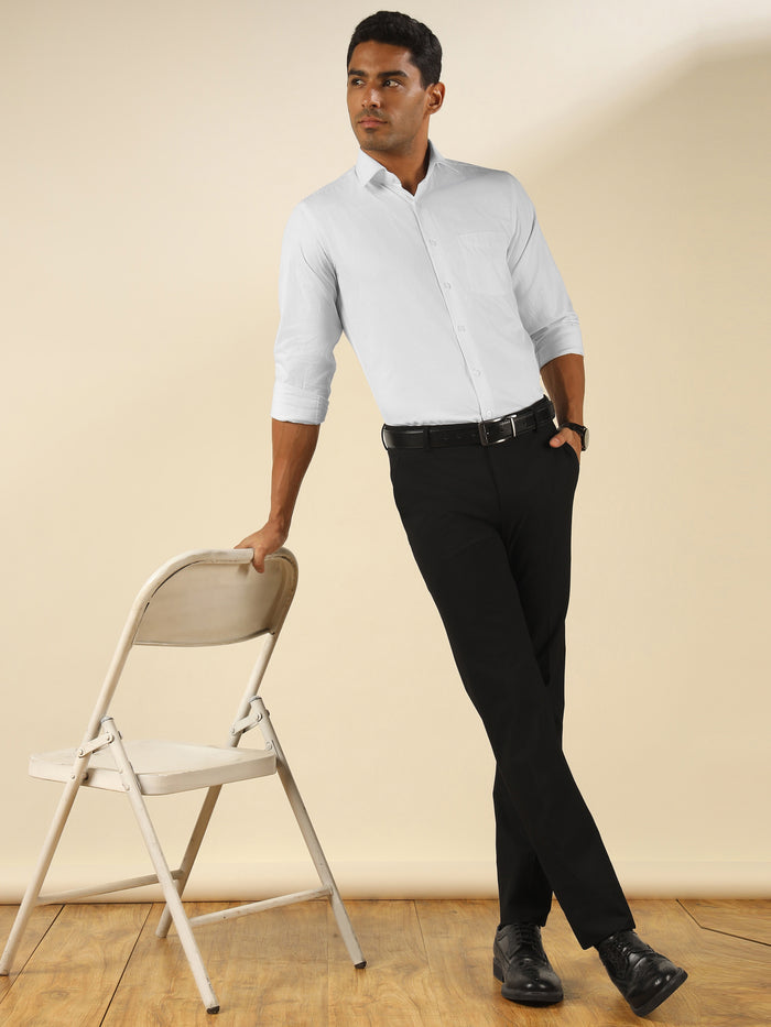 Man in white shirt and black pants standing next to a white folding chair.