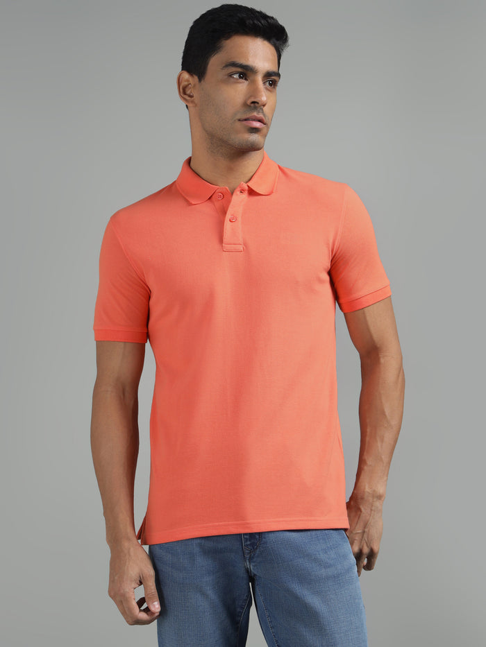A man wearing a coral pink, regular fit, solid polo neck t-shirt with short sleeves.