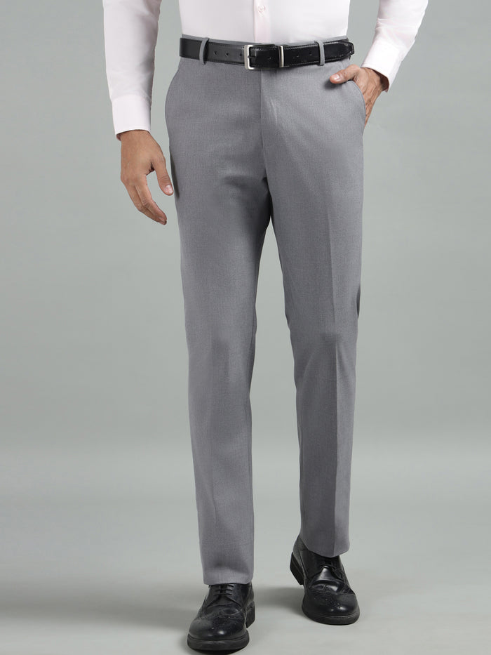 A man wearing grey straight fit trousers with a white shirt and black shoes.