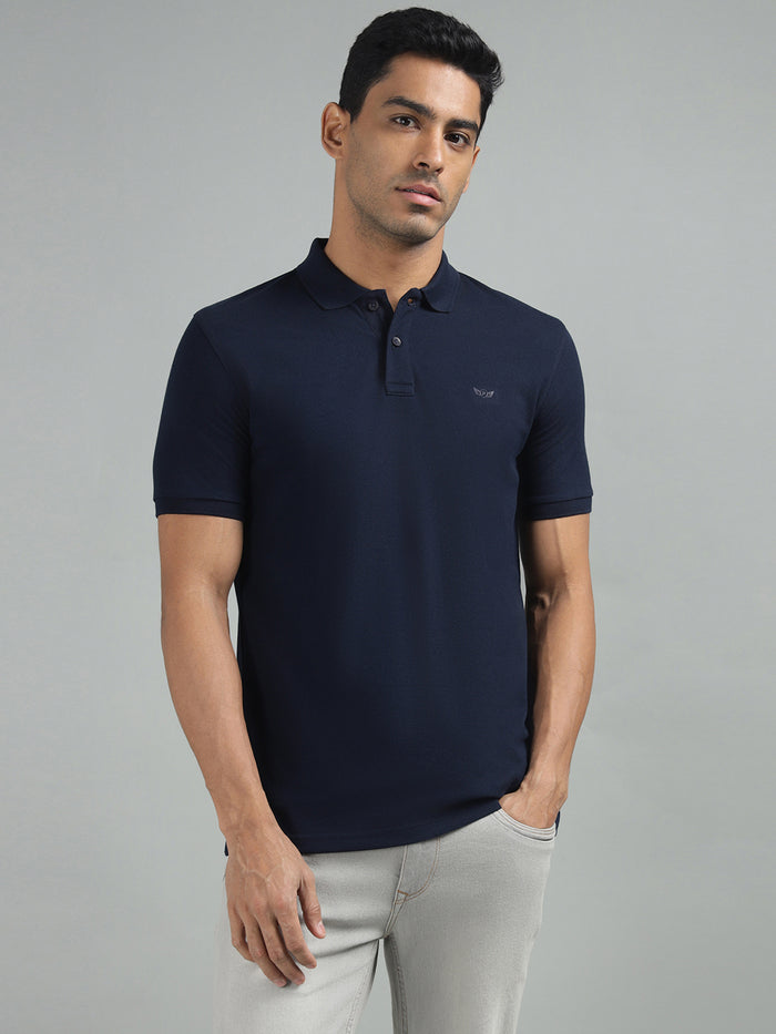 A man wearing a navy blue regular fit solid polo neck t-shirt with short sleeves, paired with light-colored trousers.