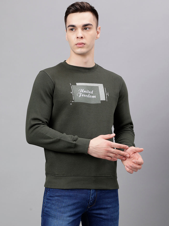 A man wearing an olive green long-sleeved crew neck sweatshirt with text on the front.