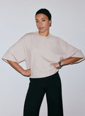 Nainen yllään hiekanvärinen Luxe Boxy Short Sleeve -toppi ja mustat housut, kädet lanteilla [M-170cm]