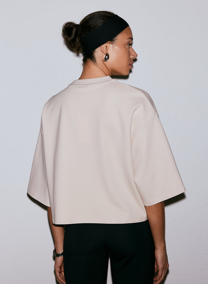 Nainen takaapäin yllään hiekanvärinen Luxe Boxy Short Sleeve -t-paita ja musta hiuspanta [M-170cm]