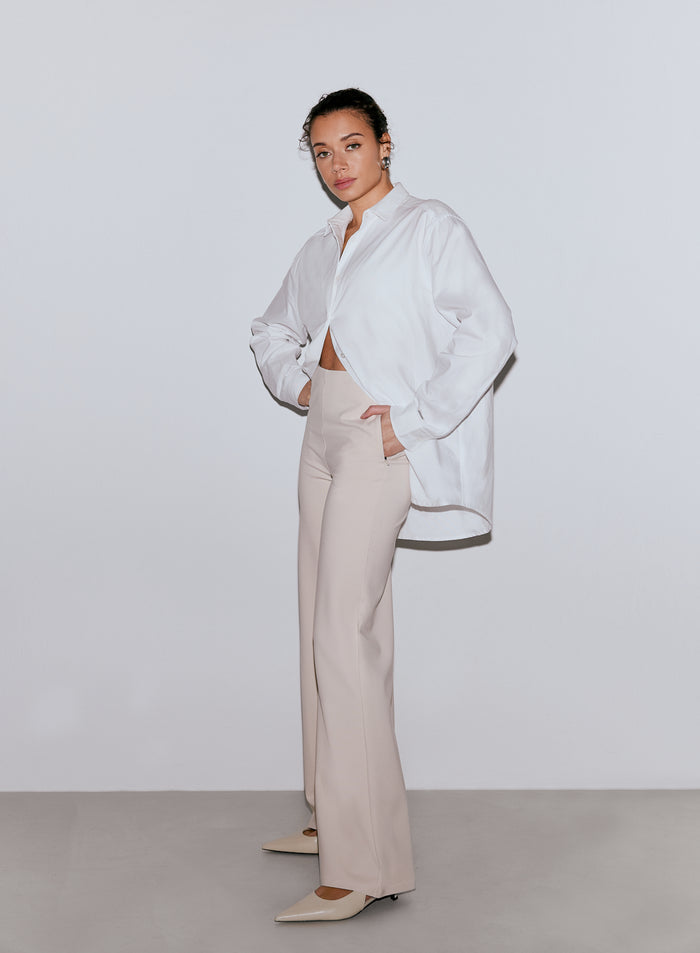 Nainen poseeraa yllään hiekanväriset Luxe Pants -housut ja valkoinen paita [36-170cm]