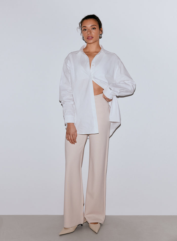 Nainen yllään valkoinen ylisuuri paita ja hiekanväriset leveälahkeiset Luxe Pants -housut [36-170CM]