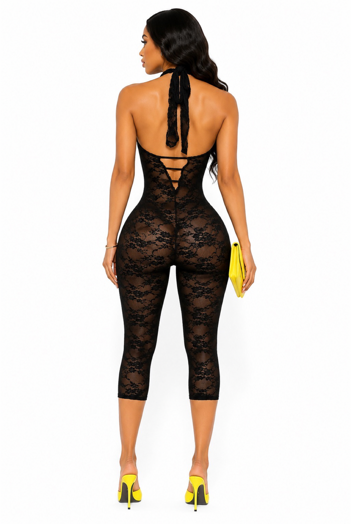 Back view of black halter lace capri romper featuring open back, tie neck detail, sheer floral lace, and bodycon silhouette.