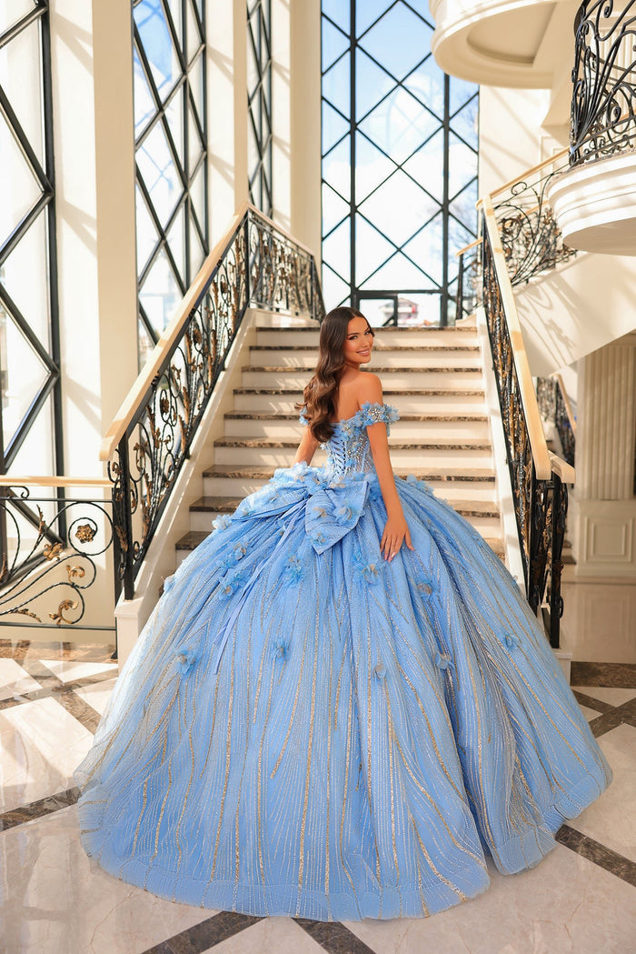 A woman in a blue off-shoulder ballgown stands on marble stairs with ornate iron railings.