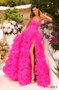 A model wears a voluminous neon pink tulle gown with a high slit, standing amid pink and purple flowers.