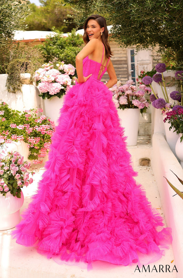 A woman in a hot pink ruffled ball gown poses in a garden surrounded by flowers.