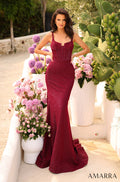 A burgundy fitted mermaid gown with corset bodice, posing amid pink flowers and green cactus.