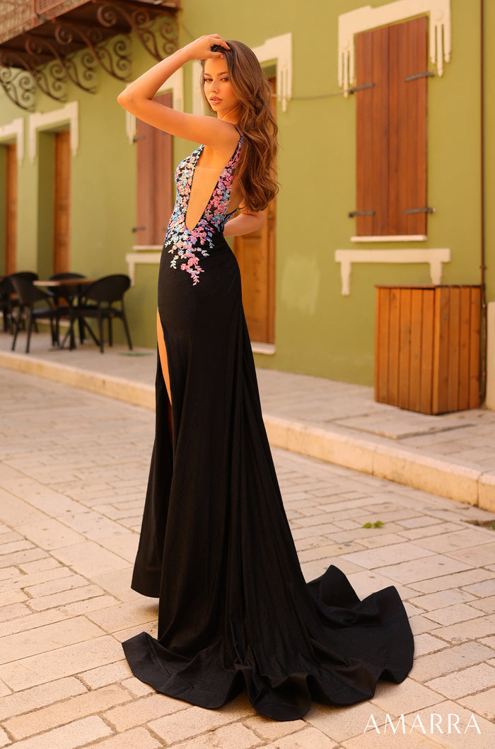 A long black evening gown with floral embellishments and a high slit, styled on a cobblestone street with green walls.