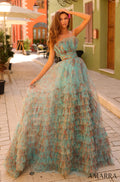 A woman wears a tiered teal and coral tulle ball gown on a cobblestone street with colorful buildings.