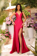A woman in a vibrant pink gown with a high slit stands among pink and purple flowers on a sunny terrace.