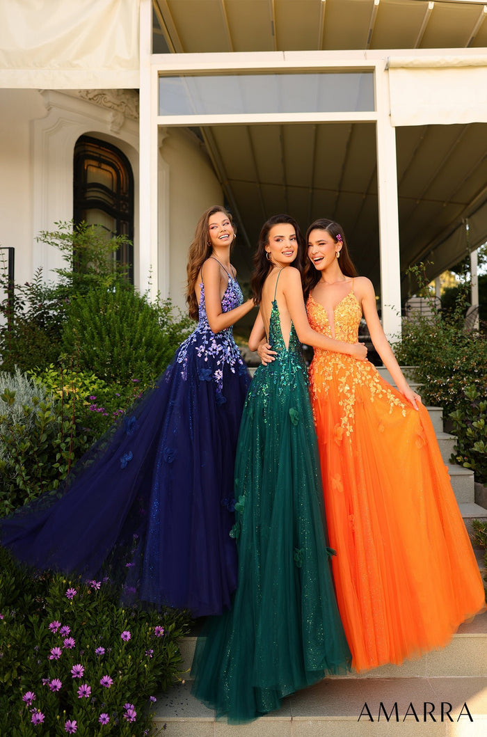 Three women wear colorful embellished ball gowns in navy, emerald green, and orange while standing together outside.