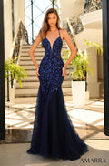 A navy blue lace mermaid gown with a deep v-neckline, worn on a model posing on a marble staircase.