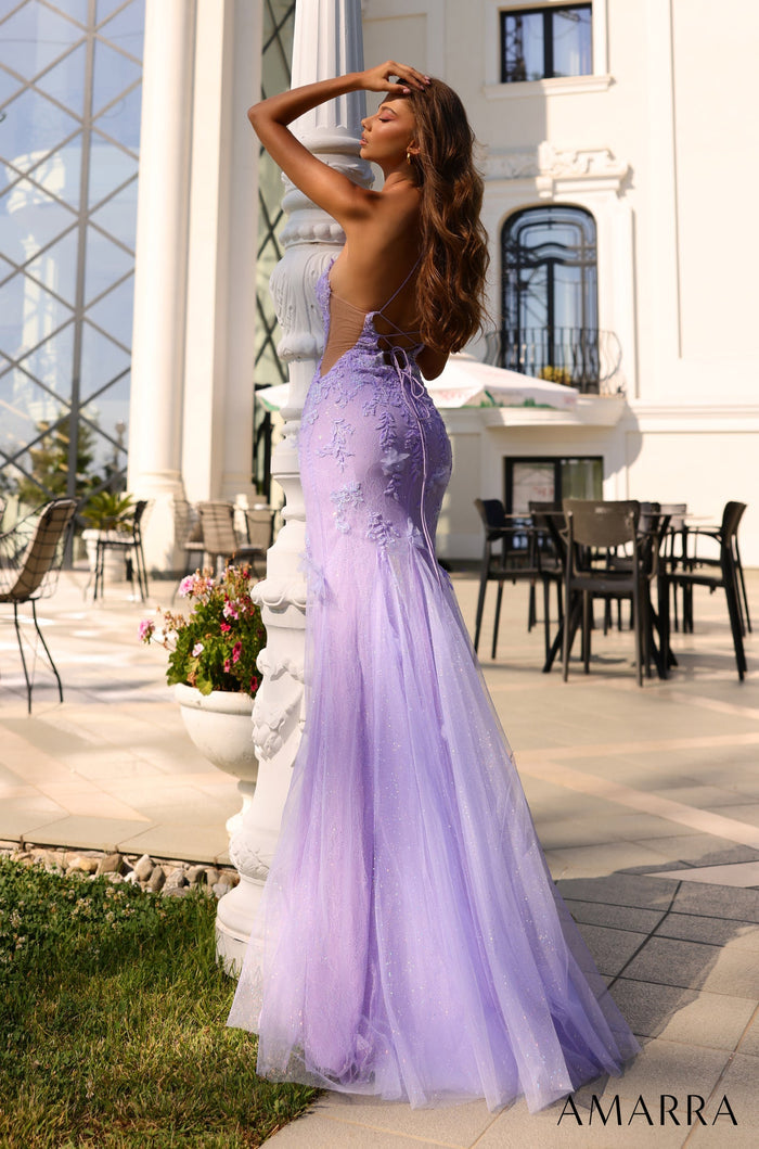 A woman in a lavender mermaid-style gown poses elegantly near white columns and outdoor seating.
